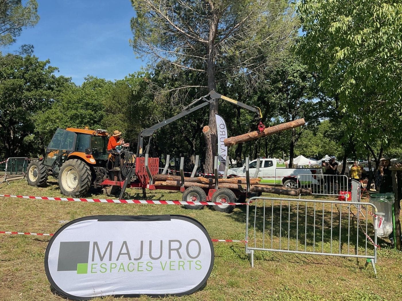 Tracteur Majuro et remorque forestière en démonstration de grutage au salon de la ruralité de Saint-Gély-du-Fesc, banderole de l’entreprise au premier plan